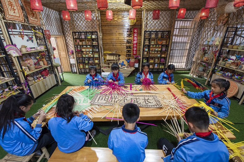 5、2021年11月25日，在广西梧州岑溪市市南渡镇中心小学，学生在老师的辅导下练习非遗竹芒编织手工技艺。（何华文）