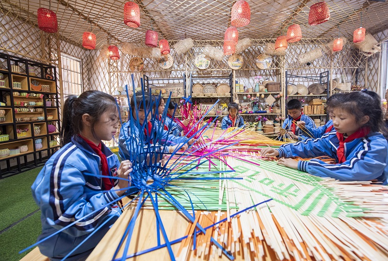 10、2021年11月25日，在广西梧州岑溪市市南渡镇中心小学，学生在老师的辅导下练习非遗竹芒编织手工技艺。（何华文）