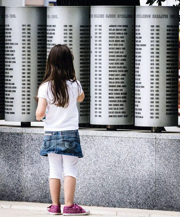 小姑娘站在刻有512名儿童死难者名字的纪念转桶前