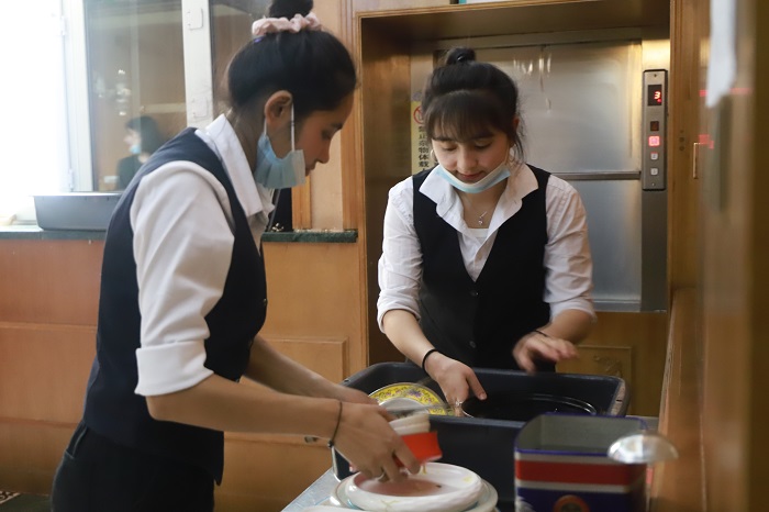 来自和田墨玉县的一餐厅领班穆开热姆·如则巴柯（右）和祖丽阿娅·图尔荪托合提（左）正在一起清理餐具。