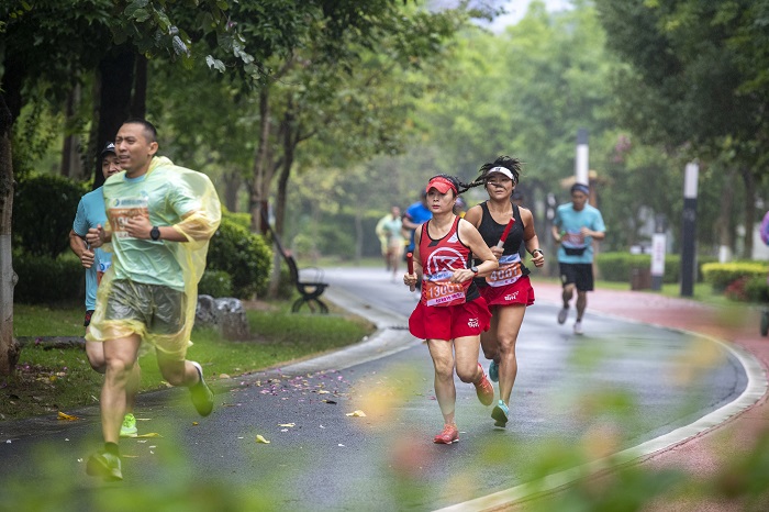 3、2022年5月22日，在广西梧州市玫瑰湖公园的步道上，梧州市畅跑跑步俱乐部会员冒雨参加运动趣味接力赛。（何华文）