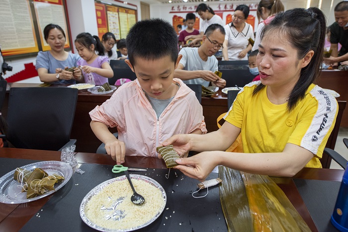 2、2022年5月28日，在广西梧州市青少年宫，孩子们在家长指导下学包粽子，迎接端午节的到来。（何华文）