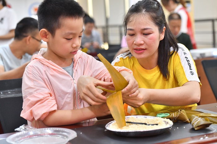 5、2022年5月28日，在广西梧州市青少年宫，孩子们在家长指导下学包粽子，迎接端午节的到来。（何华文）