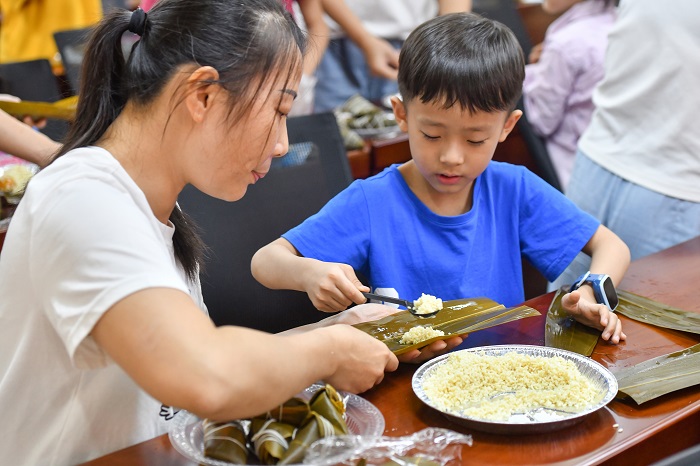 8、2022年5月28日，在广西梧州市青少年宫，孩子们在家长指导下学包粽子，迎接端午节的到来。（何华文）