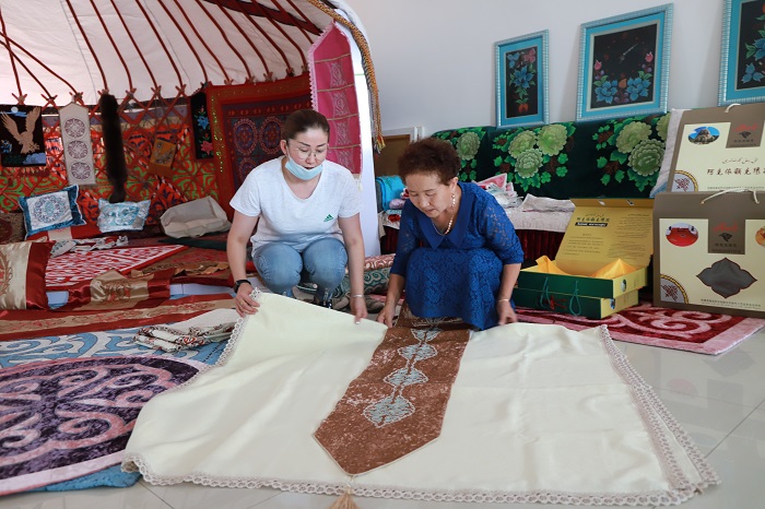 富蕴县阿克依额克民族刺绣专业合作社高级民间艺术师库力拉·依曼别克正在向顾客介绍刺绣产品。 (1)