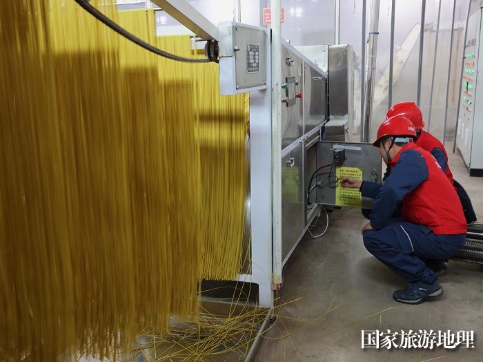 除了烙锅，岩脚古镇当地的小麦面条也是驰名远近，供不应求。流水线作业的机器设备离不开稳定的电力供应。“柳岸水乡”电力服务队会定时在古镇大大小小的面条生产企业走访检查，帮助他们解决用电问题。（熊倩  摄）