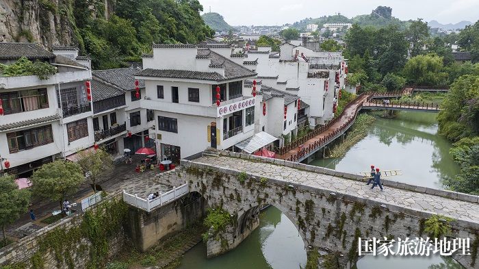 南网贵州六盘水六枝供电局岩脚供电所成立“柳岸水乡”服务队，针对古镇景区电力保障，以网格经理为基础，实行24小时随诊的全天候服务。图为供电员工行走在古镇两百余年历史的三合桥上。