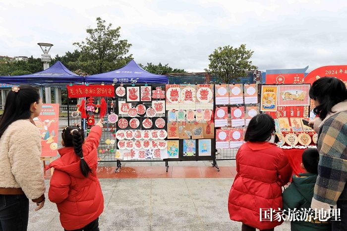 图9：1月20日，在广西柳州市融安县长安广场，家长和学生在非遗集市上欣赏作品。（谭凯兴 摄）