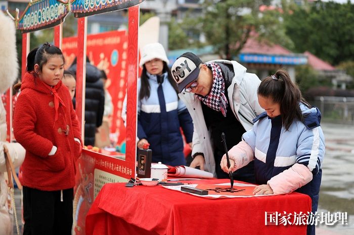 图10：1月20日，在广西柳州市融安县长安广场，一名小学生在书写福字，准备赠送市民。（谭凯兴 摄）