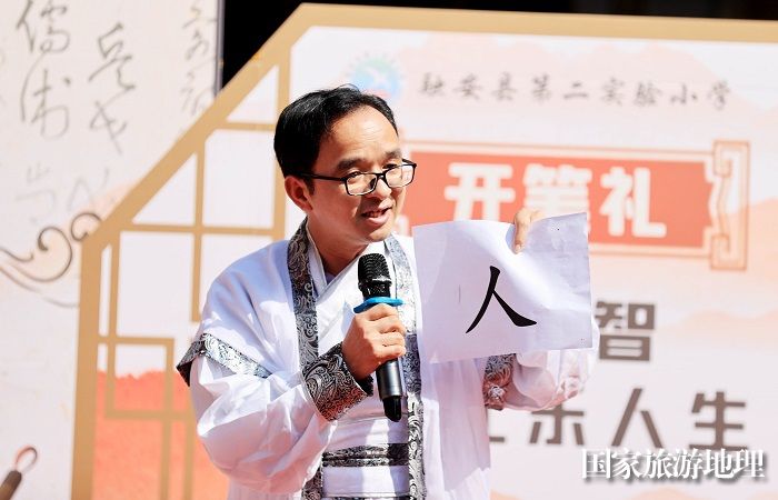 图8：3月11日，在广西柳州市融安县长安镇骑楼街，一名老师在“开笔礼”仪式上讲解书写人字的意义。（谭凯兴 摄）