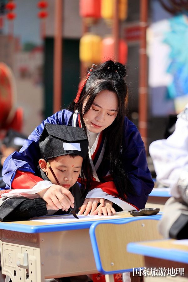 图10：3月11日，在广西柳州市融安县长安镇骑楼街，一名老师在“开笔礼”仪式上手把手教学生书写人字。（谭凯兴 摄）